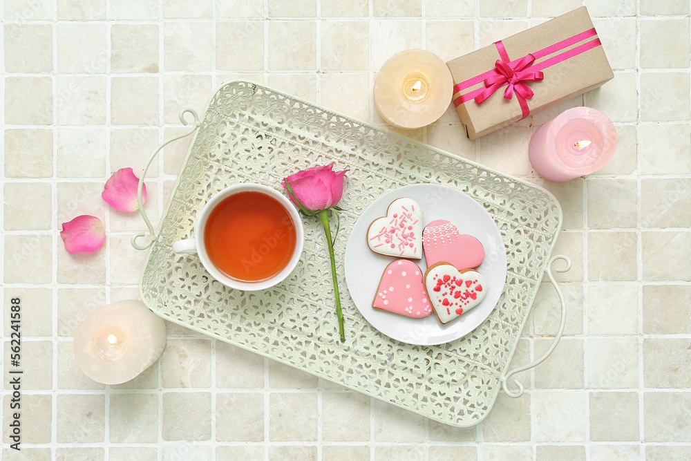 Composition with tasty heart shaped cookies, cup of tea, gift box and burning candles on light tile. Valentine's Day celebration Composition with tasty heart shaped cookies, cup of tea, gift box and burning candles on light tile. Valentine's Day celebration