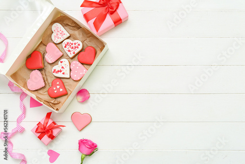 Box with tasty heart shaped cookies, gifts and rose flower on light wooden background. Valentine's Day celebration