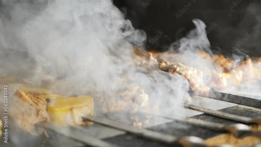 thick smoke in the process of baking a delicious meat barbecue with golden pieces of potatoes is strung on metal skewers in the grill of a restaurant kitchen. thick smoke in the process of baking a delicious meat barbecue with golden pieces of potatoes is strung on metal skewers in the grill of a restaurant kitchen.