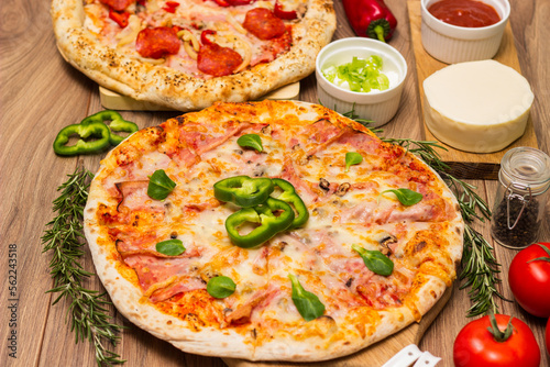 Two different pizza with ingredients on rustic background. Pepperoni pizza and pizza Capricciosa with mozzarella cheese, ham, tomato sauce, salami, mushroom, pepper, spices and fresh basil