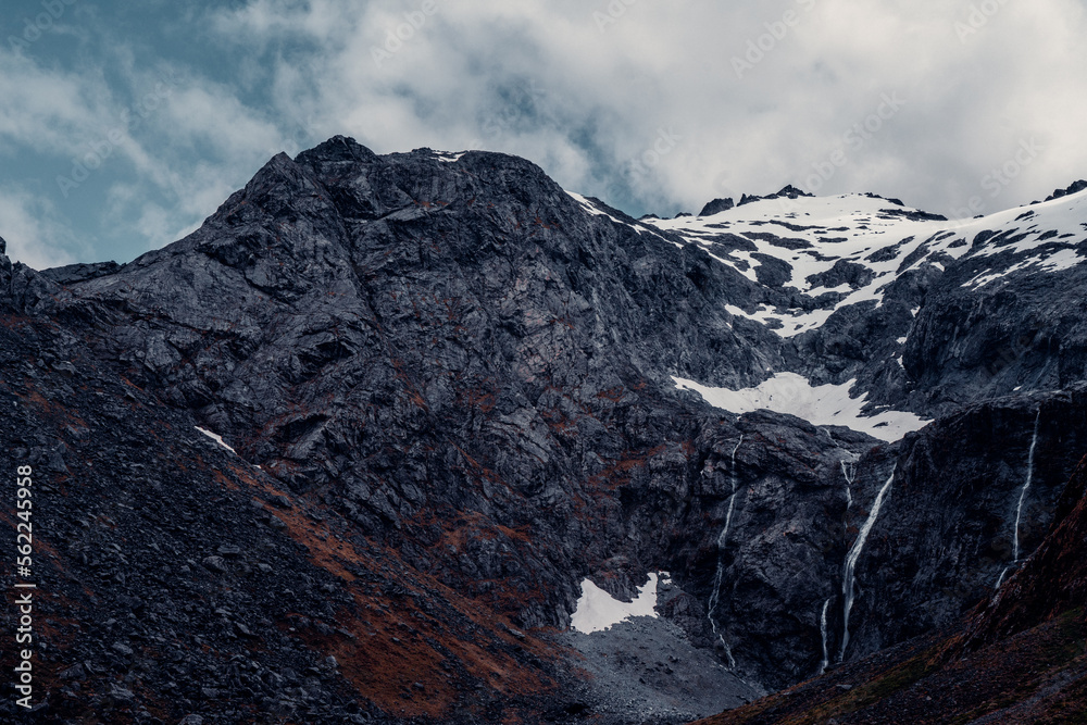 Obraz premium Landscape Shot of Water From Melting Glaciers Above, Cascades off Side of Mountain in New Zealand