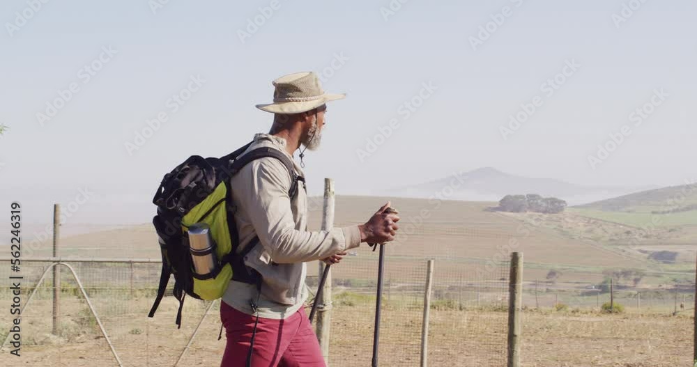 Senior african american man hiking with trekking poles on sunny day, slow motion