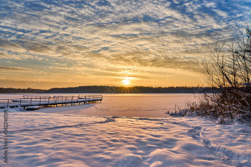 Sunset clouds over frozen lake. Sunset colors reflection in snow covered lake. Frozen lake pier on sunset