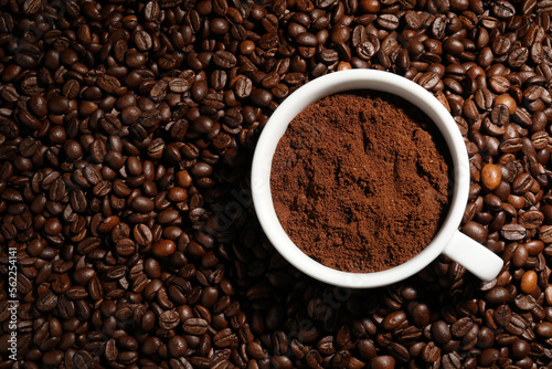 Cup with ground coffee on roasted beans, top view. Space for text