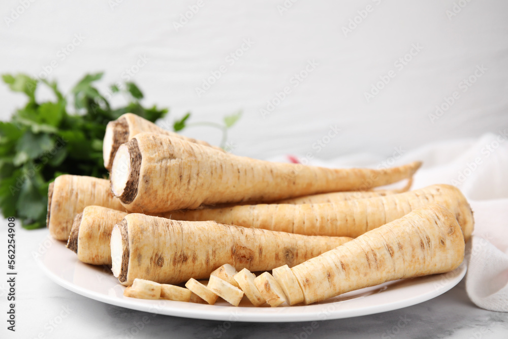 Plate with whole and cut parsley roots on white table, closeup Plate with whole and cut parsley roots on white table, closeup