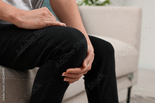 Woman suffering from knee pain on sofa indoors, closeup. Arthritis symptoms