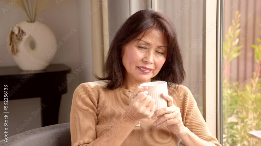 Attractive woman waves to camera holding coffee cup relaxing near bright home window Attractive woman waves to camera holding coffee cup relaxing near bright home window