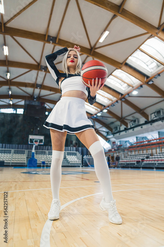 Low angle full shot of a cheerleader posing with a basketball in a gymnasium. Sport concept. Vertical photo. High quality photo