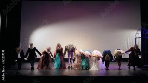Group of performers holding hands walking on stage bowing and clapping. Wide shot portrait of talented Caucasian actors and actresses in elegant retro-style costumes thanking in theater after show photo