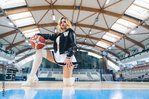 Low angle shot of a cheerleader kneeling on one knee and holding a basketball in her hand. Sport concept. High quality photo