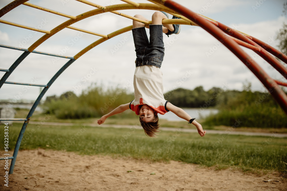 happy teen boy enjoy childhood by hanging upside down from pole of a  climbing frame on playground Stock Photo | Adobe Stock