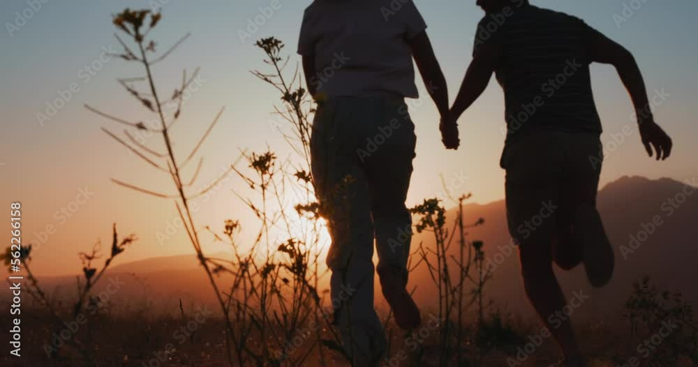Silhouette of couple running in a mountain field at sunset, holding hands, young and romantic family enjoying. Back view slow motion