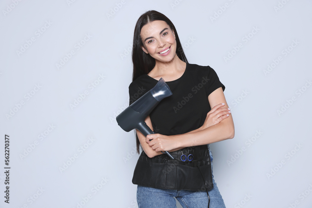 Portrait of happy hairdresser with hairdryer and professional tools on light background