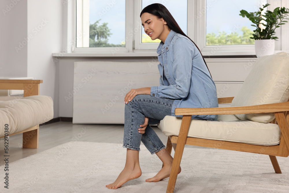 Woman suffering from leg pain on armchair at home Woman suffering from leg pain on armchair at home