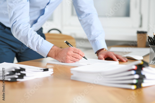 Man working with documents at wooden table in office, closeup