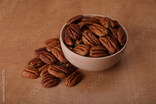 Bowl and tasty pecan nuts on wooden table