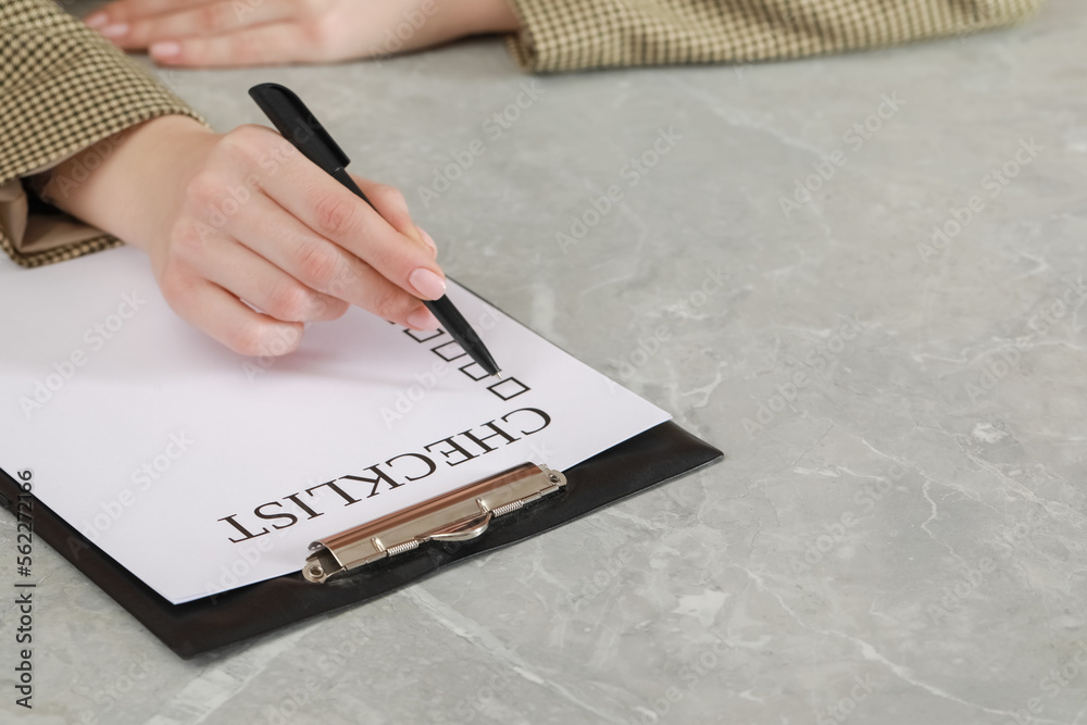 Woman filling Checklist at grey marble table, closeup. Space for text Woman filling Checklist at grey marble table, closeup. Space for text