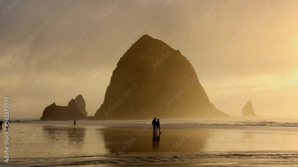 People enjoying beautiful sunset over Oregon coastline. Cinematic landscape of idyllic Cannon Beach with low tides crashing against the shore. High quality 4k footage