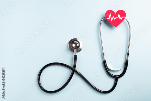 Heart health and medical concept. Medical stethoscope and cardiogram on red heart on pastel blue background. Top view, flat lay, copy space