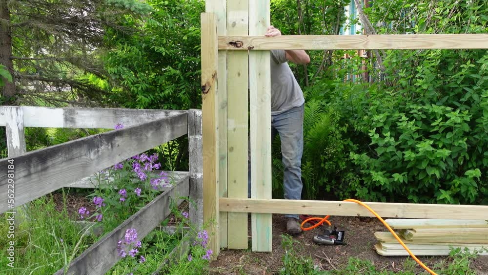 Man prepares plank and fix it with pneumatic nail gun for fence, static view Man prepares plank and fix it with pneumatic nail gun for fence, static view
