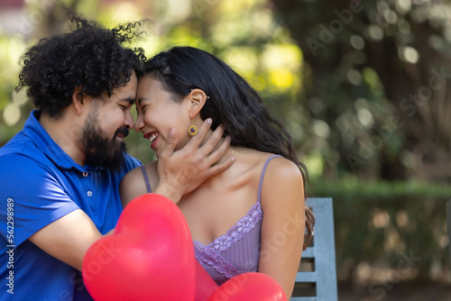 mexican young latin couple laughing and talking on valentine s day  with red heart shaped balloons
