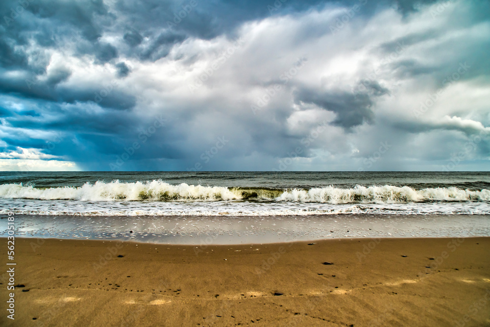 A sandy seashore with clouds. Background with the sky and the surf on the theme of beach holidays and sea travel.