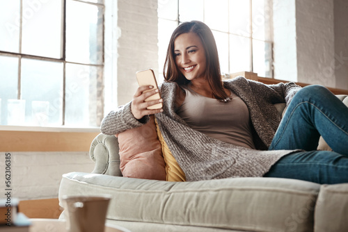 Woman, phone and relax on sofa for social media, app and text in her home, happy and smile. Girl, smartphone and app for chatting, online dating and internet, search and entertainment in living room photo
