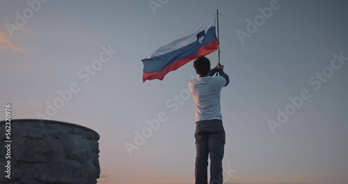 Camera circling aroud the hiker at the top of mountain Peca holding a pol with a slovenian flag attached on it, fluttering in the wind. photo