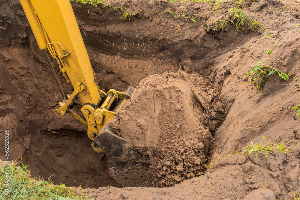 A bucket of excavator with a pile of earth digs a hole on the construction site. Industrial work A bucket of excavator with a pile of earth digs a hole on the construction site. Industrial work