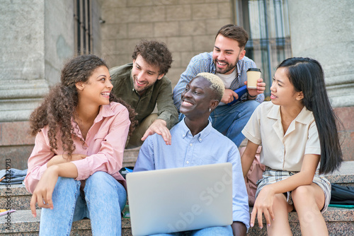 multi-racial group of students with a laptop discussing the news.