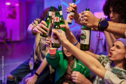 Close-up of hands of young intercultural people toasting with green bottles of beer at home party while celebrating life event