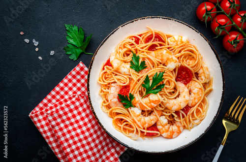 Spaghetti pasta with shrimp, cherry tomatoes, olive oil and parsley in plate on black table background. Top view, copy space