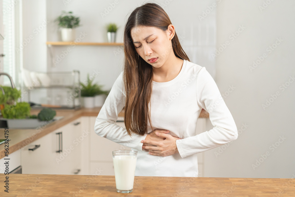 Pain, suffering asian young woman having a stomachache, abdominal pain or digestive, hand in holding belly after drink glass of milk. Lactose intolerance, allergy from dairy food, health care problem. Pain, suffering asian young woman having a stomachache, abdominal pain or digestive, hand in holding belly after drink glass of milk. Lactose intolerance, allergy from dairy food, health care problem.