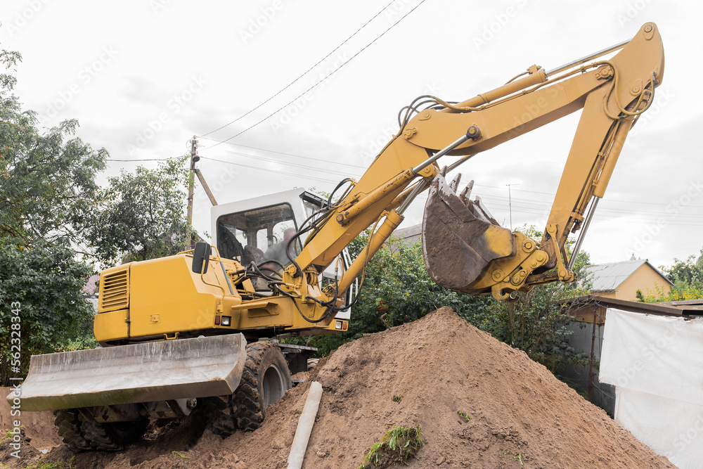 A hydraulic piston and a bucket excavator dig the ground next to a pile of sand on an industrial site A hydraulic piston and a bucket excavator dig the ground next to a pile of sand on an industrial site