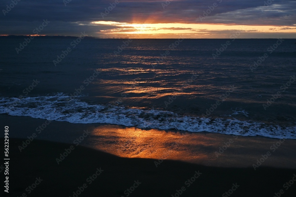 The beach at dawn when the sun's rays dye the waves red. Japanese natural background material.