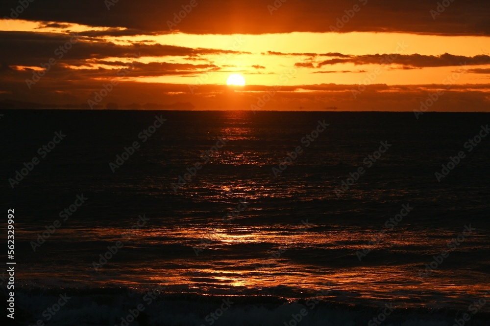 Fototapeta premium The beach at dawn when the sun's rays dye the waves red. Japanese natural background material.