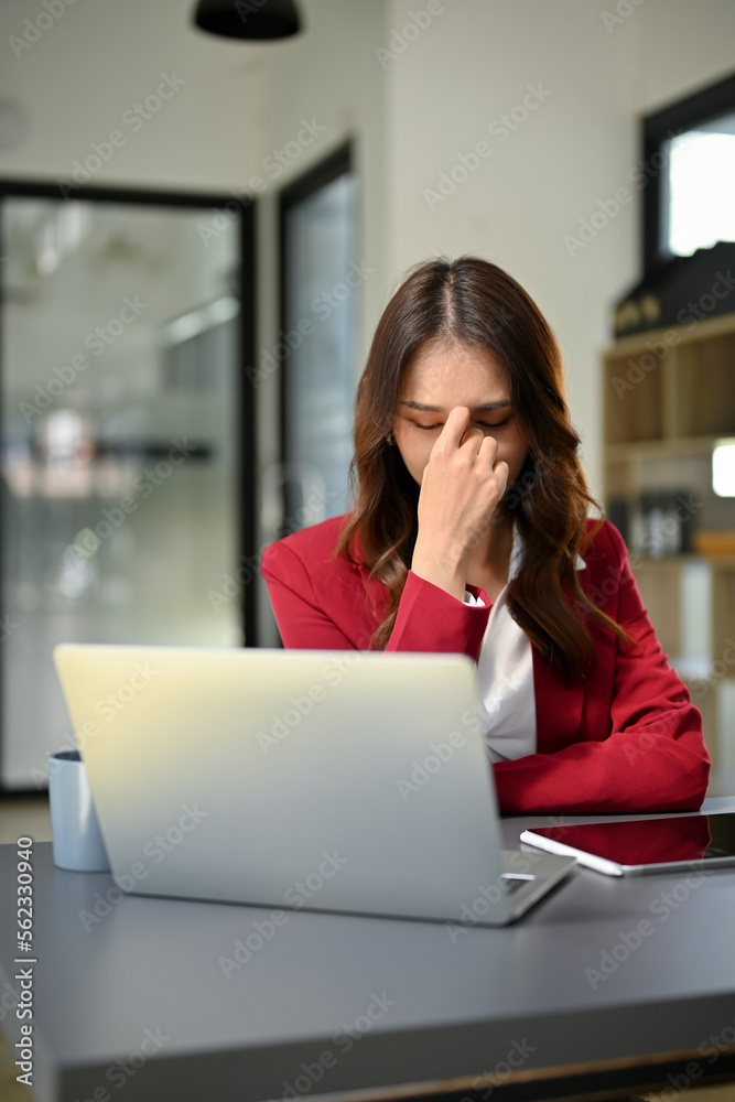 Stressed and depressed Asian businesswoman sits at her office desk, suffering from eyes strain
