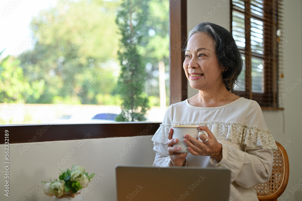 Happy aged Asian businesswoman working from home, looking out the window and daydreaming Happy aged Asian businesswoman working from home, looking out the window and daydreaming