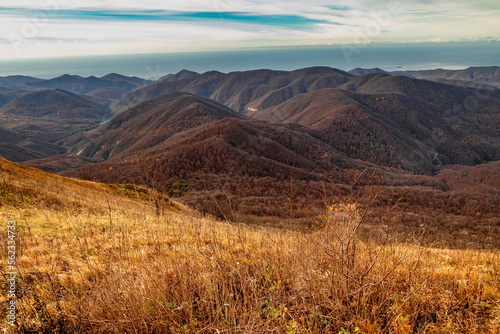 Stunning view from the rocky peak of Mount Peus to the mountain peaks of the Caucasus on a sunny day with blue sky and dramatic clouds. View from a height of 1000 m to the peaks of the Caucasus. 