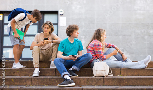 Group of teens gathered together on stairs beside school building and using their smartphones.