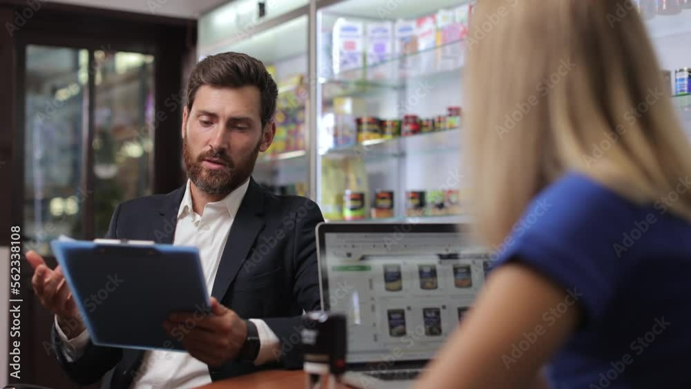 Side view of business partners making agreement, talking, discussing in office. Man with beard wearing costume, reading, looking through contract, talking with woman. Concept of business. Side view of business partners making agreement, talking, discussing in office. Man with beard wearing costume, reading, looking through contract, talking with woman. Concept of business.