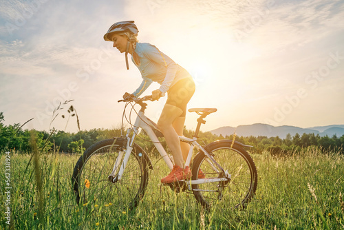 Fototapeta Naklejka Na Ścianę i Meble -  Cyclist Woman riding bike in helmets go in sports outdoors on sunny day a mountain in the forest. Silhouette female at sunset. Fresh air. Health care, authenticity, sense of balance and calmness.