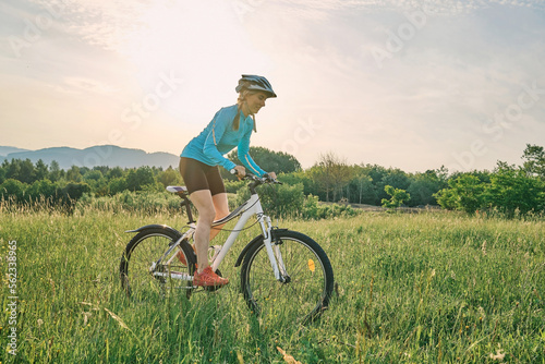 Fototapeta Naklejka Na Ścianę i Meble -  Cyclist Woman riding bike in helmets go in sports outdoors on sunny day a mountain in the forest. Silhouette female at sunset. Fresh air. Health care, authenticity, sense of balance and calmness.