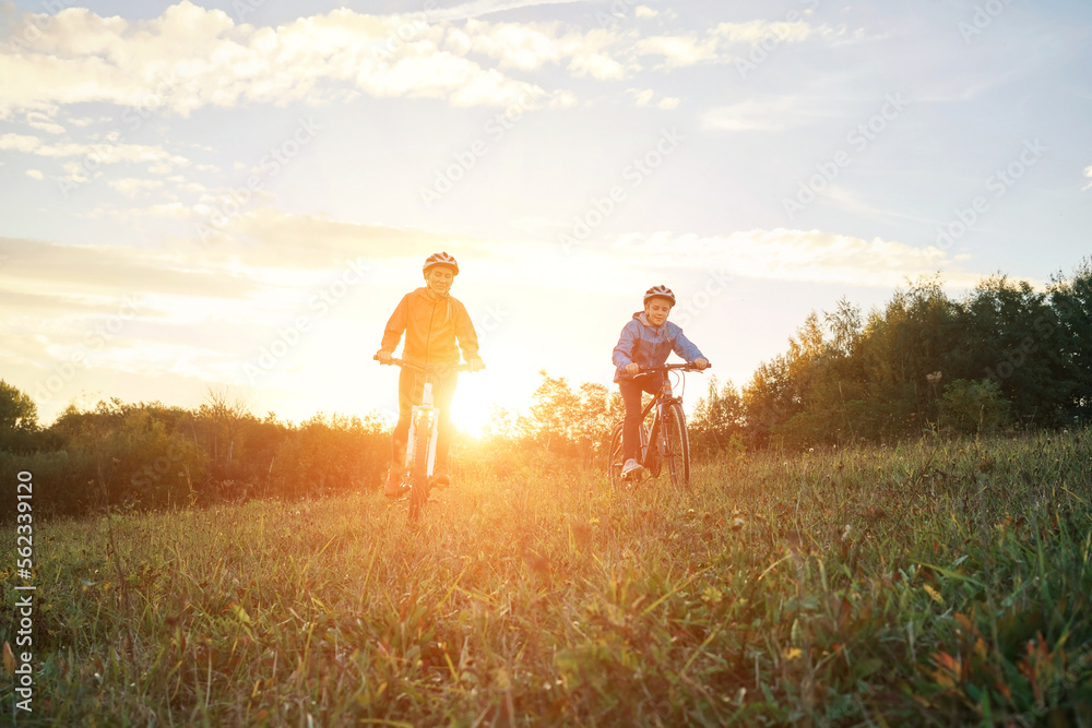 Mother and son ride a bike. Happy cute boy in helmet learn to riding a bike in park on green meadow in autumn day at sunset time. Family weekend.
