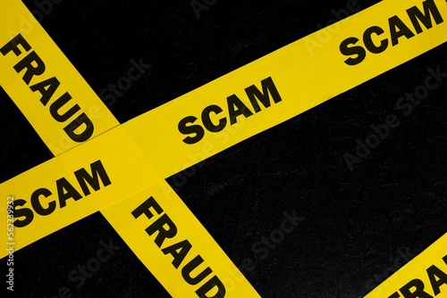 Scam and fraud alert, caution and warning concept. Yellow barricade tape with word scam in dark black background.
