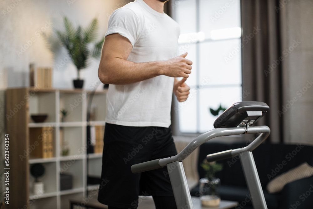 Concept of health and morning workout. Close up view of part of body of young sportsman running on treadmill on the background of modern stylish house. Concept of health and morning workout. Close up view of part of body of young sportsman running on treadmill on the background of modern stylish house.