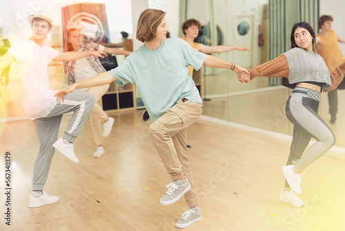 Sporty cheerful teenagers learning to dance vigorous jive in pairs in choreography class.