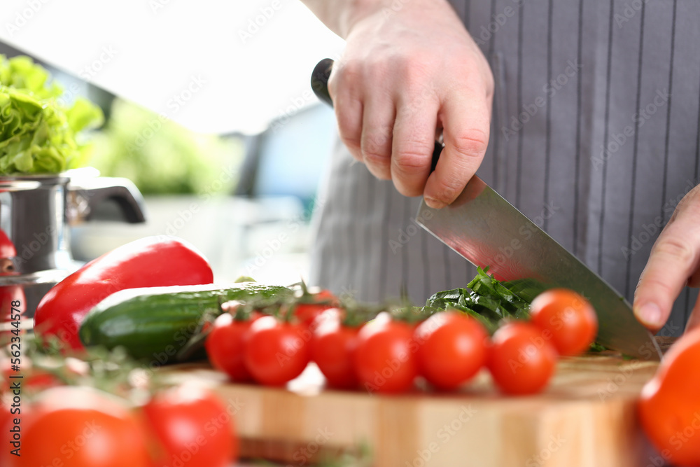 Cook cuts tomatoes and cucumbers on cutting board Cook cuts tomatoes and cucumbers on cutting board
