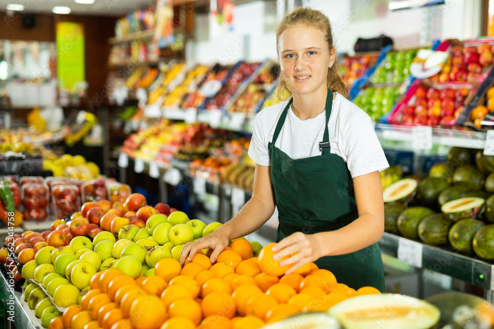 Portrait of teenage girl working in grocery shop as job experience, selling ripe oranges