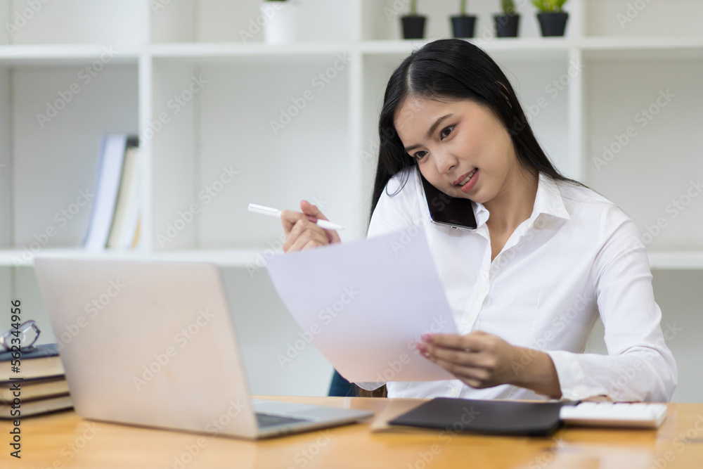 Busy businesswoman working on laptop and talking on phone in office analyzing monthly work schedule. Busy businesswoman working on laptop and talking on phone in office analyzing monthly work schedule.